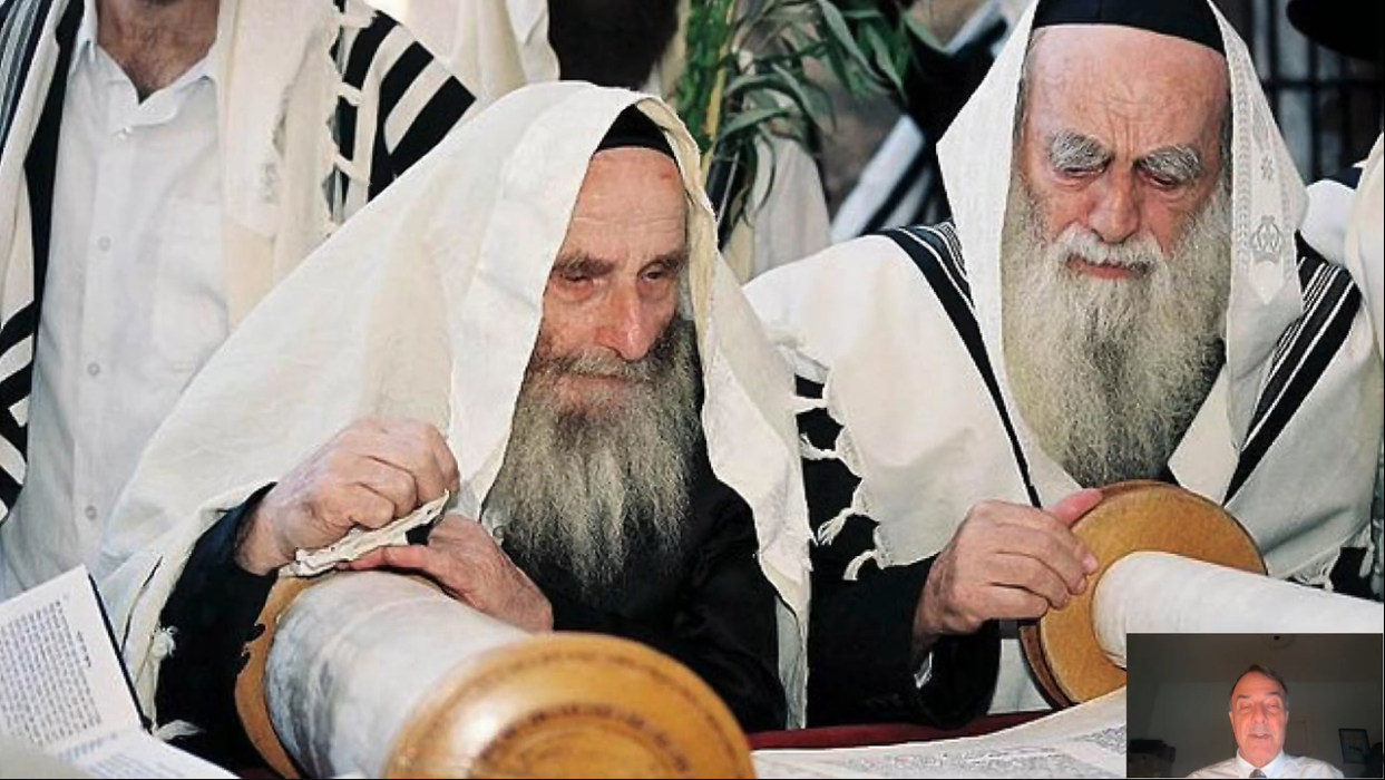 Photograph of two bearded Jewish men wearing prayer shawls and reading an open Torah scroll.